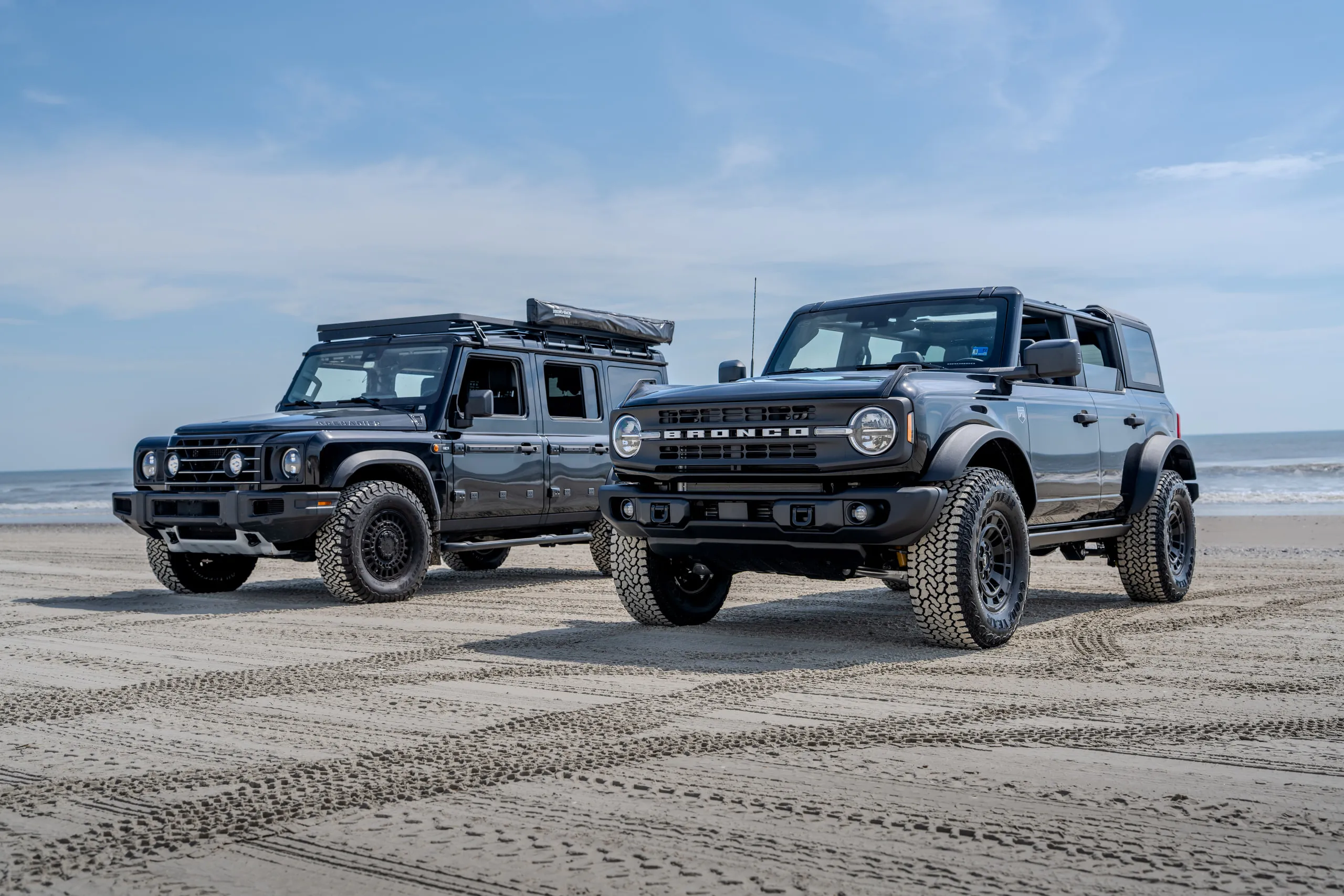 Two kitted-out four-by-fours parked side by side on hard-packed sand by the sea